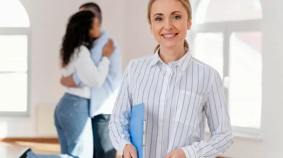 front-view-of-smiley-female-realtor-with-young-couple-embracing-in-the-backgroun