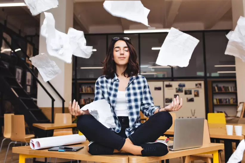 young-pretty-joyful-brunette-woman-meditating-on-table-surround-work-stuff-and-flying-papers-cheerful-mood-taking-break-working-studying-relaxation-tr