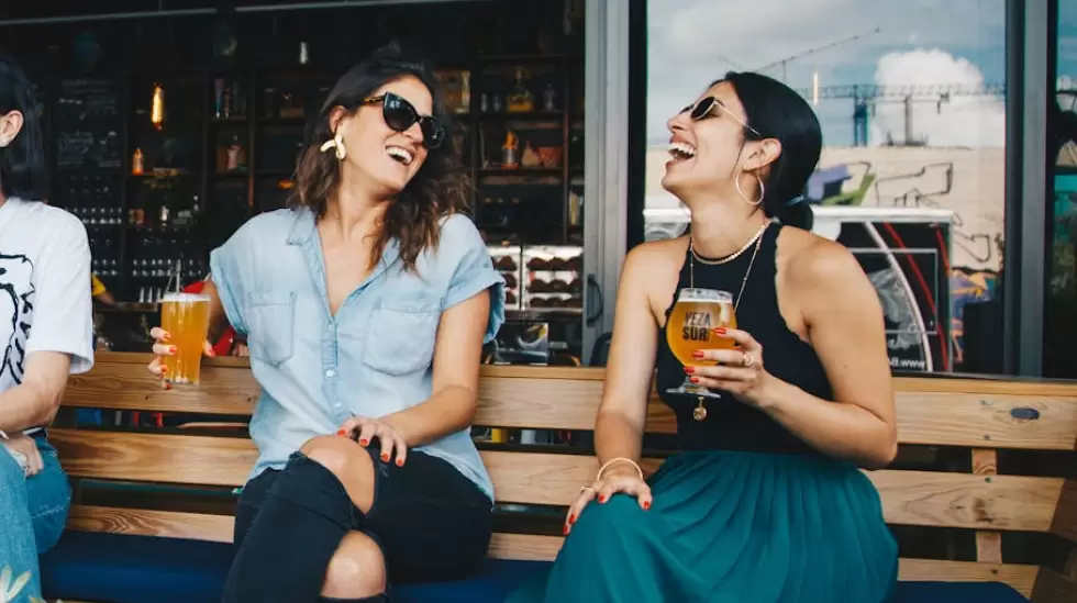 Dos Mujeres Sonrientes Sentadas En Un Banco De Madera