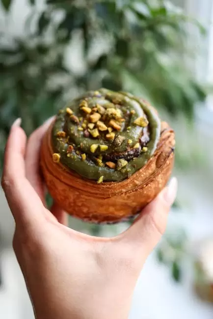 Delicioso panecillo de canela cubierto de pistachos, mantenido al aire libre, que muestra su textura.