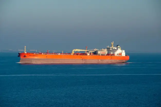 Un barco transportador de GNL de color naranja brillante navega por aguas tranquilas del mar en un día claro.