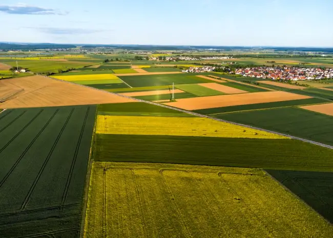 Imagen aérea que muestra un mosaico vibrante de tierras de cultivo con un pueblo en la distancia, bajo un cielo azul claro. (Foto. Pexels)