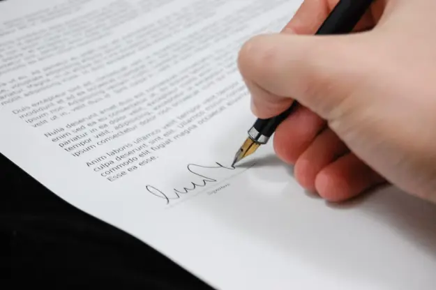 Primer plano de una mano firmando un documento legal con una pluma, simbolizando firma y acuerdo. (Foto: Pexels)