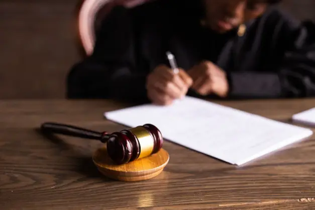 Juez firmando documentos en el escritorio con enfoque en el mazo, representando la ley y la justicia. (Foto: Pexels)