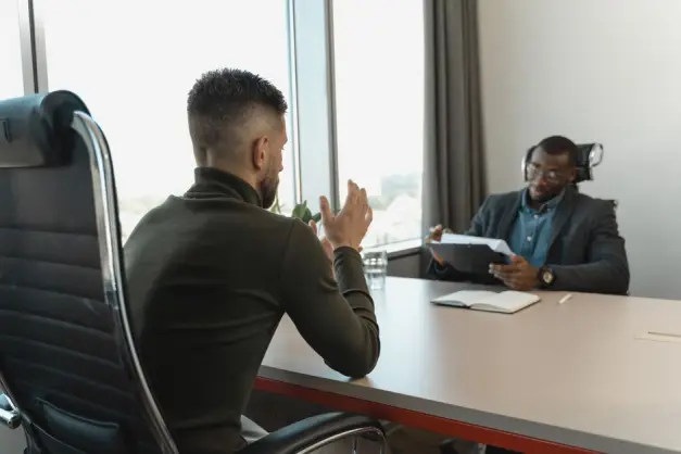 Dos hombres en un entorno de entrevista de trabajo en una oficina moderna con grandes ventanas. (Foto: Pexels)