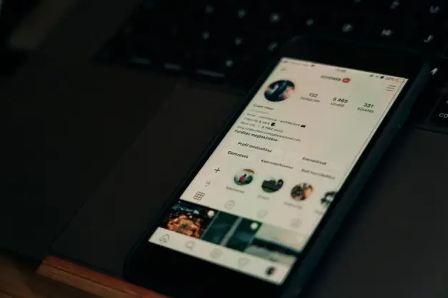 Primer plano de un smartphone mostrando una pantalla de perfil de redes sociales junto a un portátil. (Foto: Pexels)