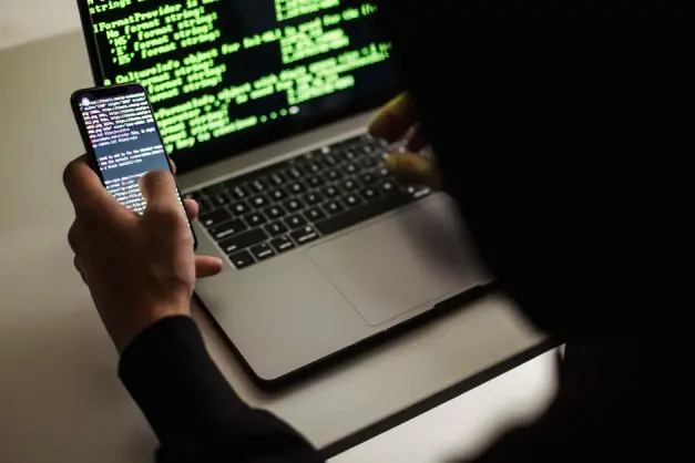 Un desarrollador codificando en un laptop y un smartphone simultáneamente en un entorno interior.