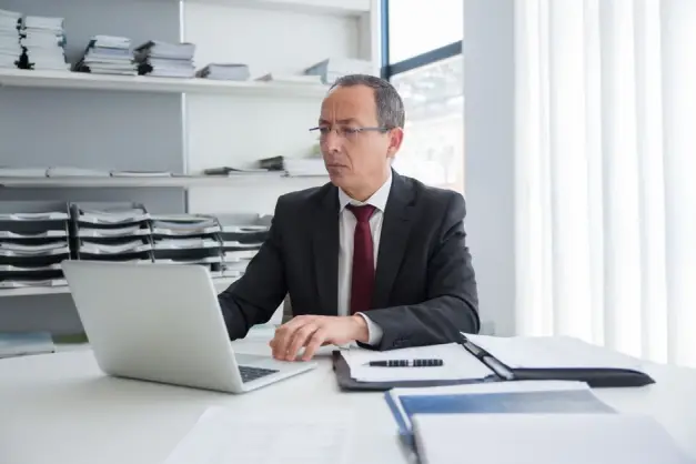 Empresario concentrado en un traje trabajando en su escritorio con un portátil y documentos. (Foto: Pexels)