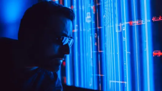 Un hombre con gafas de sol estudia atentamente una pantalla holográfica azul vibrante, simbolizando tecnología digital. (Foto: Pexels)