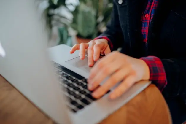 Manos escribiendo en el teclado de un portátil, vista cercana, en un entorno interior informal. (Foto: Pexels)