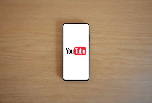 Vista desde arriba de un smartphone mostrando el logotipo de YouTube sobre una superficie de madera, mostrando la tecnología moderna.