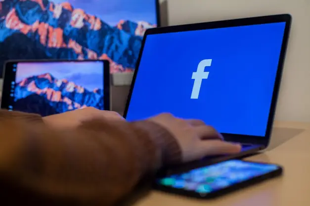 Portátil mostrando Facebook en un espacio de trabajo con múltiples dispositivos, destacando la tecnología moderna. (Foto: Pexels)