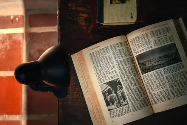 Ambiente cálido de biblioteca con un libro abierto y una lámpara de escritorio en iluminación suave. (Foto: Pexels)