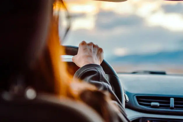 Primer plano de la mano de una mujer en el volante mientras conduce con una vista escénica delante. (Foto: Pexels)