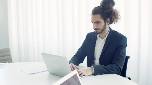 Empresario con recogido escribiendo en el portátil en una oficina moderna y luminosa. (Foto: Pexels)