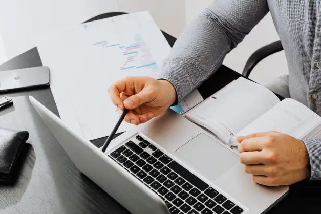 Profesional usando laptop y revisando documentos en el escritorio para análisis de datos. (Foto: Pexels)