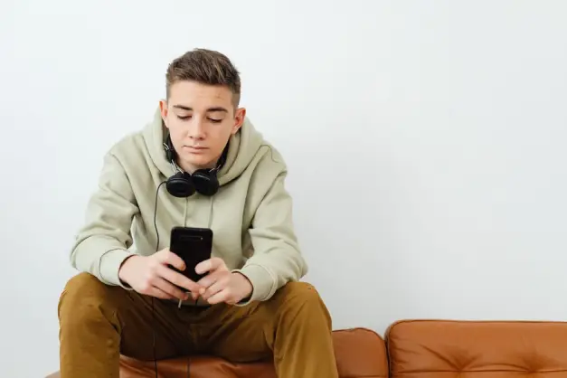 Joven adulto relajándose con un smartphone y auriculares en un sofá en un ambiente relajado. (Foto: Pexels)