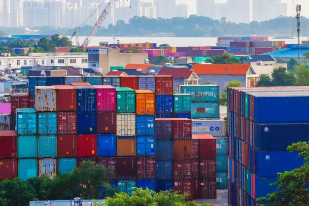 Contenedores de carga apilados vibrantes en un puerto bullicioso con el horizonte urbano de fondo. (Foto: Pexels)
