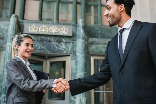 Dos profesionales de negocios dándose la mano con confianza fuera de un edificio moderno. (Foto: Pexels)