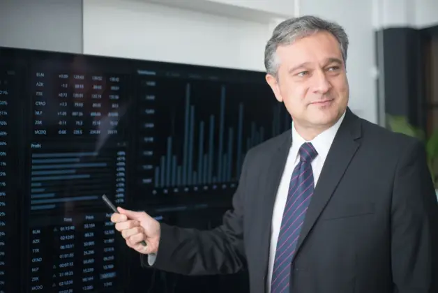 Hombre profesional con traje revisando gráficos financieros en el monitor, mostrando tendencias del mercado de valores. (Foto: Pexels)