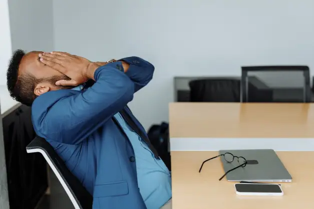 Un empresario estresado con traje se cubre la cara mientras está sentado en un escritorio con herramientas de oficina. (Foto: Pexels)