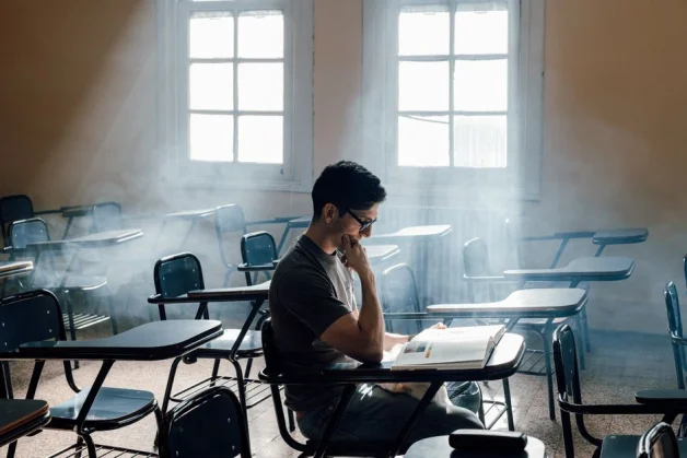 Estudiante concentrada mientras escribe durante un examen en un aula iluminada.