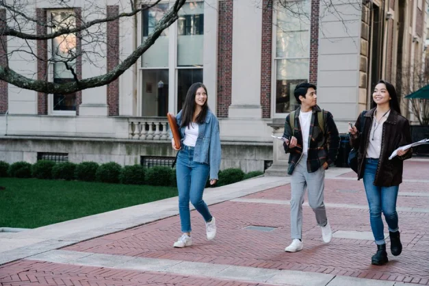 Grupo de jóvenes estudiantes camina por un sendero dentro de un campus universitario durante el día.