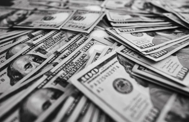 Imagen monocromática de billetes de cien dólares estadounidenses dispersos que representan riqueza y prosperidad.