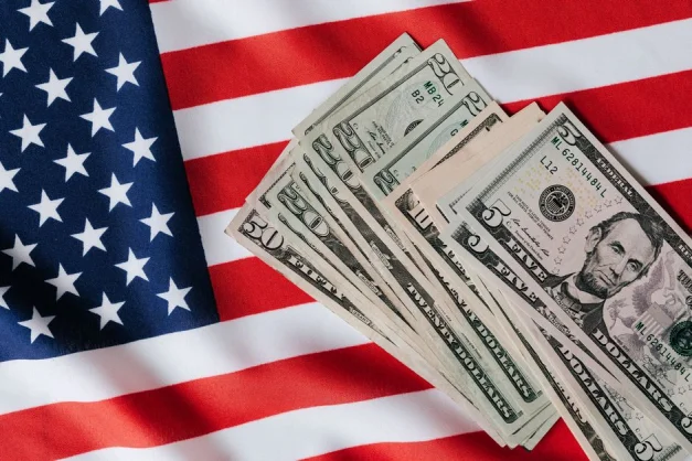 Un montón de billetes de dólar de EE.UU. colocados sobre la bandera americana, simbolizando economía y patriotismo.