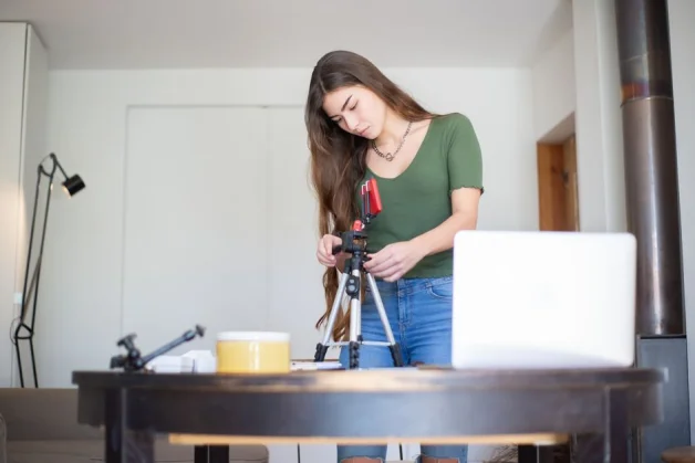 Joven mujer configurando una cámara en trípode en un acogedor estudio interior, lista para vlogging o fotografía.