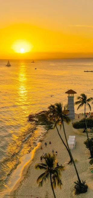 Atardecer dorado sobre la playa de Bayahíbe con un faro y palmeras, evocando vibras de paraíso tropical.
