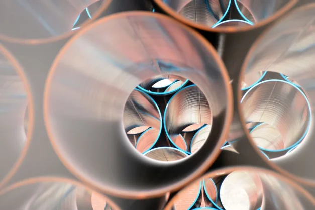 Perspectiva artística de tubos de acero apilados que crean un patrón geométrico con reflejos.