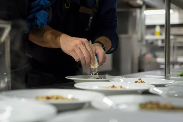Un chef ralla parmesano sobre platos bellamente dispuestos en una cocina de restaurante de alta gama.