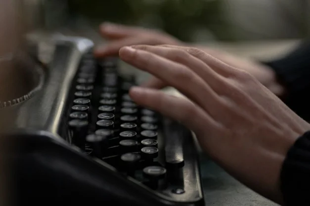 Acercamiento de manos escribiendo en una máquina de escribir antigua, evocando nostalgia y creatividad.