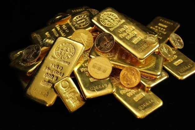 Un primer plano de lingotes y monedas de oro que simbolizan riqueza e inversión sobre un fondo negro.