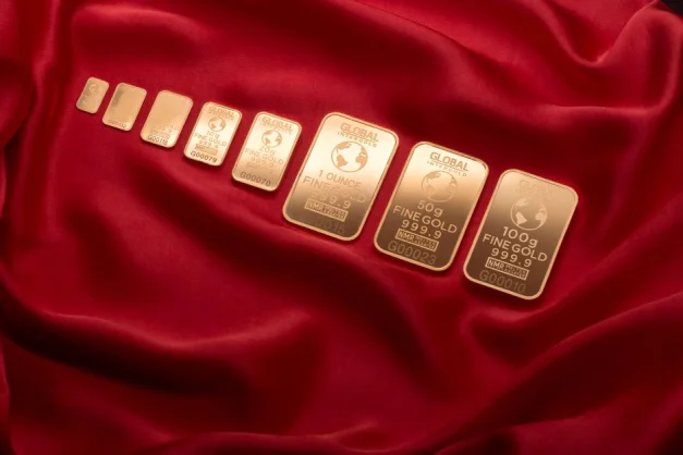 Array de finas barras de oro exhibidas sobre una rica tela roja, simbolizando riqueza y lujo.