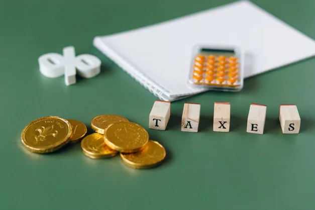 Acercamiento de artículos relacionados con impuestos, incluyendo monedas, calculadora y la palabra 'impuestos' sobre un fondo verde.