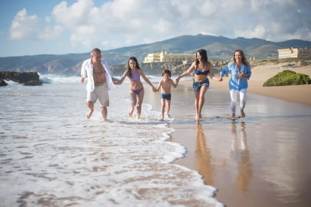 Una familia corriendo en una playa pintoresca en Portugal, de la mano y disfrutando de las olas.