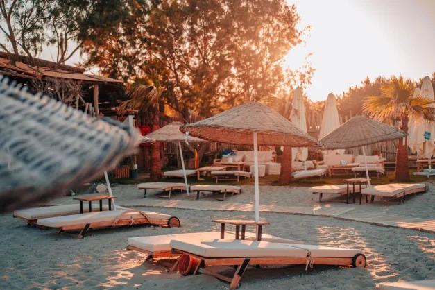 Escena de playa relajante al atardecer con tumbonas y sombrillas en una atmósfera cálida y tranquila.