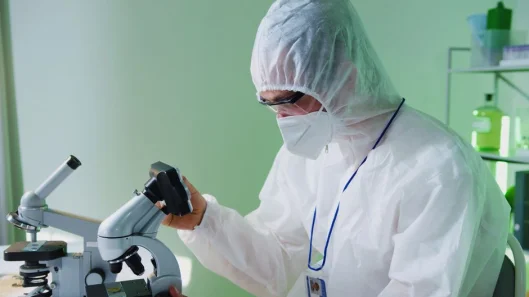 Un científico con equipo de protección examina muestras bajo un microscopio en un laboratorio.