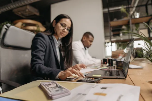 Dos profesionales de negocios colaborando con un portátil y una calculadora en una oficina moderna.