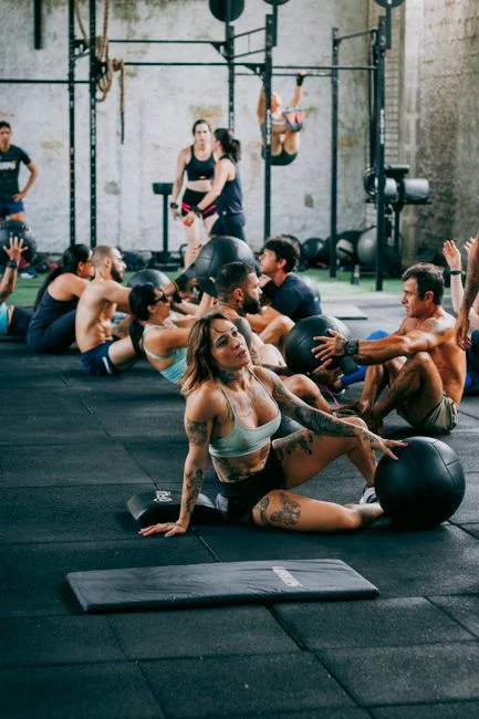 Un grupo diverso de adultos participando en una intensa clase de fitness utilizando pelotas medicinales en interiores.
