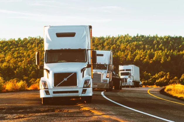 Tres camiones de semi-remolque circulando por una autopista en un paisaje forestal en Arizona.