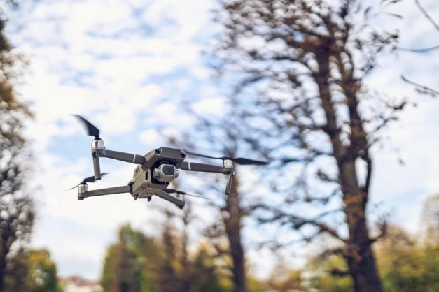 Drone en vuelo entre árboles con un fondo de cielo despejado, mostrando tecnología y naturaleza.