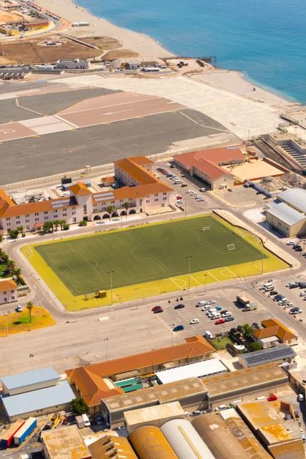 Fotografía aérea de un campo deportivo costero y una pista cercana junto al mar.
