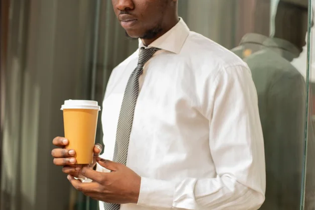 Hombre profesional sosteniendo un vaso de café desechable en un entorno de oficina moderno.
