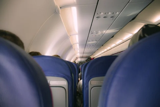 Una vista de una cabina moderna de avión que muestra filas de asientos azules y compartimentos superiores.