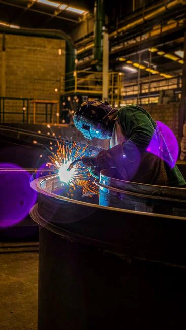 Un soldador experto trabajando con chispas intensas en un entorno de fábrica poco iluminado.