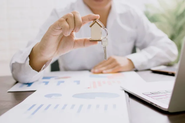 Profesional inmobiliario presentando un modelo de casa con llaves, simbolizando inversión y propiedad.