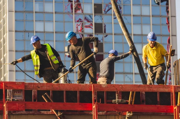 Un grupo de obreros de la construcción, equipados con trajes de seguridad, trabajan activamente en la construcción de un edificio de gran altura.